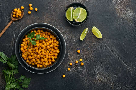 Fried chickpeas with turmeric with parsley and lime in black plate on an old black table background....
