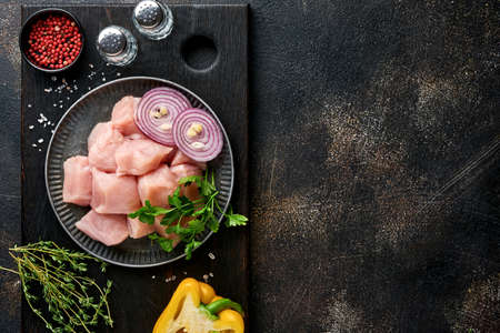 Raw pieces meat ingredients of chicken on wooden board, spices, herbs and vegetables on dark gray...