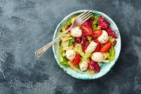 Mozzarella, tomato and mix of fresh salad leaves, slate stone table background, top view. Mock up.の写真素材