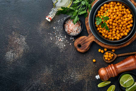 Fried chickpeas with turmeric with parsley and lime in black plate on an old black table background. Roasted spicy chickpeas or Indian chana or chole, popular snack recipe. Top view.の写真素材