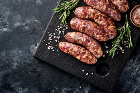 Raw sausages or bratwurst on cutting board with spices and ingredients for cooking. Top view with copy space on stone table.の写真素材