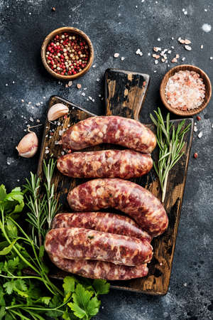 Raw sausages or bratwurst on cutting board with spices and ingredients for cooking. Top view with copy space on stone table.の写真素材