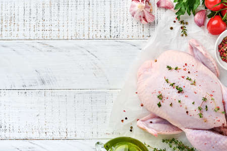 Whole raw chicken with ingredients for making pepper, lemon, thyme, garlic, cherry tomato, sorrel and salt in the kitchen on light gray slate, stone or concrete background. Top view with copy spaceの写真素材