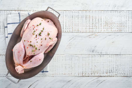 Whole raw chicken with ingredients for making pepper, lemon, thyme, garlic, cherry tomato, sorrel and salt in the kitchen on light gray slate, stone or concrete background. Top view with copy spaceの写真素材