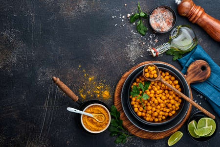 Fried chickpeas with turmeric with parsley and lime in black plate on an old black table background. Roasted spicy chickpeas or Indian chana or chole, popular snack recipe. Top view.の写真素材