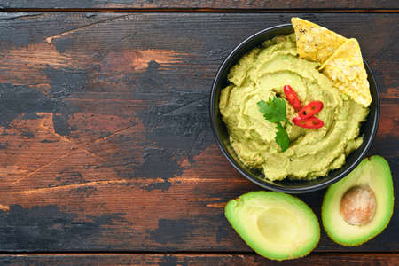 Guacamole. Traditional latinamerican Mexican dip sauce in a black bowl with avocado and ingredients and corn nachos. Avocado spread. Top view. Copyspaceの写真素材
