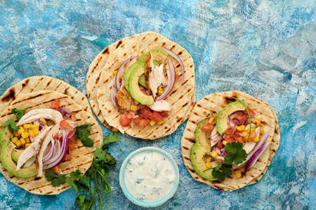 Mexican tacos with grilled chicken, avocado, corn kernels, tomato, onion, cilantro and salsa at blue...