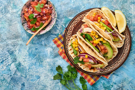 Mexican tacos with grilled chicken, avocado, corn kernels, tomato, onion, cilantro and salsa at blue stone table. Traditional Mexican and Latin american street food. Top view.の写真素材