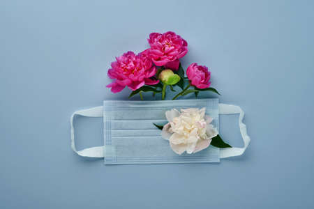Protective medical face mask with peonies flowers on blue background.