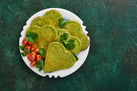 Spinach avocado pancakes in the shape of a heart with greek yogurt sauce and cherry tomatoes on a black plate over dark background. Breakfast food concept. Top view with copy space.の写真素材