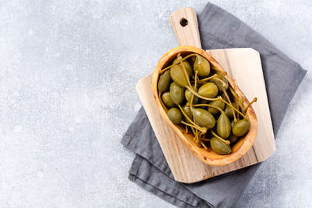 Capers canned in wooden old bowl on trendy concrete background. Top view