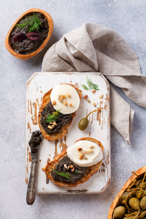 Sandwich with slice of mozzarella cheese and tapenade, caper on light gray rustic table background. Traditional Provence dish. Selective focusの写真素材