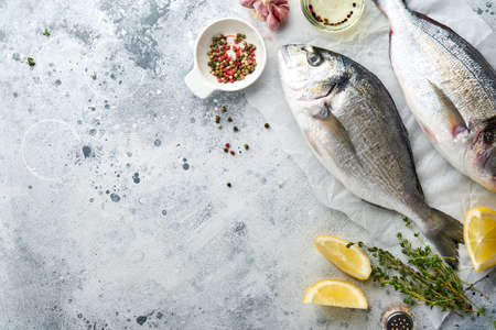 Raw dorado fresh fish or sea bream with ingredients for making lemon, thyme, garlic, cherry tomato and salt on light gray slate, stone or concrete background. Top view with copy space.の写真素材