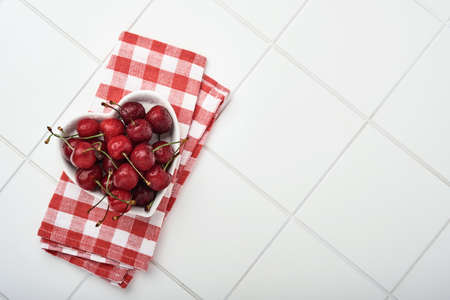 Cherry with water drops on heart shaped plate on white stone table. Fresh ripe cherries. Sweet red...