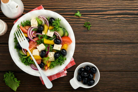 Traditional Greek salad of fresh cucumber, tomato, sweet pepper, lettuce, red onion, feta cheese and olives with olive oil on white plate. Healthy food, top view.の写真素材