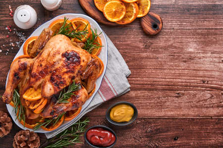 Roasted or baked whole chicken with rosemary and oranges, homemade for Christmas traditional family dinner on an old wooden rustic table. Top view with copy space.の写真素材