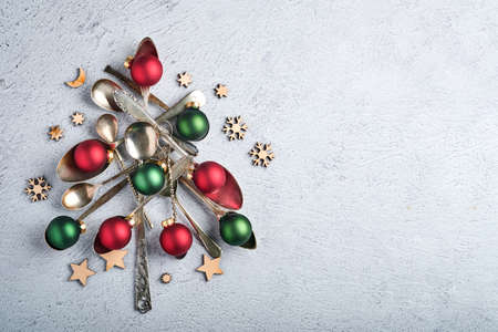 Christmas tree made from old spoons or cutlery with red and green Christmas balls on gray stone or...