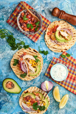 Mexican tacos with grilled chicken, avocado, corn kernels, tomato, onion, cilantro and salsa at blue...