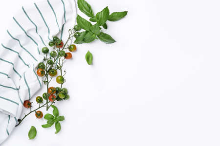 Fresh cherry tomato branches, basil leaves, napkin, pepper and pepper mill on a white background....