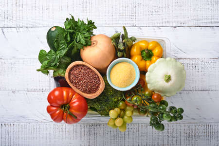Plastic box with assortment of fresh vegetables, fruits, cereals and seeds on old wooden background. Safe home delivery, food cooking and healthy clean food background and mock up.の写真素材