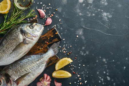 Raw dorado fresh fish or sea bream with ingredients for making lemon, thyme, garlic, cherry tomato and salt on a black slate, stone or concrete background. Top view with copy space.の写真素材
