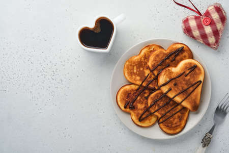 Pancakes in shape of breakfast hearts with chocolate sauce in gray ceramic plate, cup of coffee on gray concrete background. Table setting for your favorite Valentines Day breakfast. Top view copy space.の写真素材