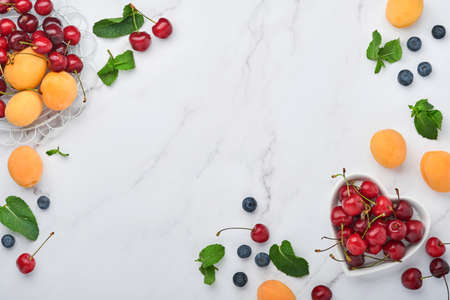 Fresh apricots, red cherry and blackberry on white marble background. Vegetarian, weight loss, clean...