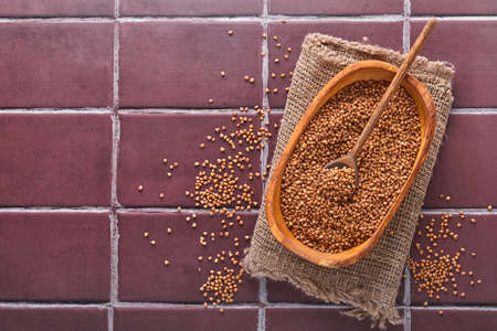 Buckwheat groats in a wooden bowl on a brown stone kitchen table. Gluten-free cereals. Top view with...