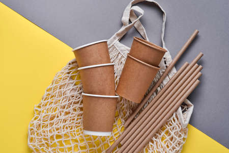 Drinking brown tubes straws made of paper and cornstarch, mesh market bag and empty paper coffee cups on a trendy gray and yellow background. Zero waste and plastic free concept. Top view.の写真素材