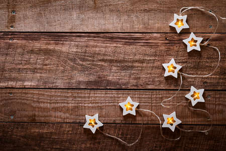 Christmas garland with wooden light stars on old dark wooden background. Top view with copy space. Christmas greeting card.の写真素材