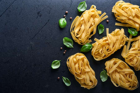 Tagliatelle. Homemade pasta, basil leaves, flour, pepper, olive oil and cherry tomato on dark black background. Food concept. Mock up. Horizontal with copy space.の写真素材