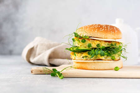 Healthy Vegetarian burger with egg and pea shoots and seeds microgreen, fresh salad, cucumber slice on a cutting wooden board on light background. Selective focusの写真素材