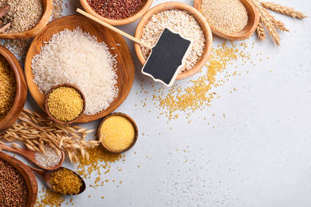 White, brown and red rice, buckwheat, millet, corn groats, quinoa and bulgur in wooden bowls on the...