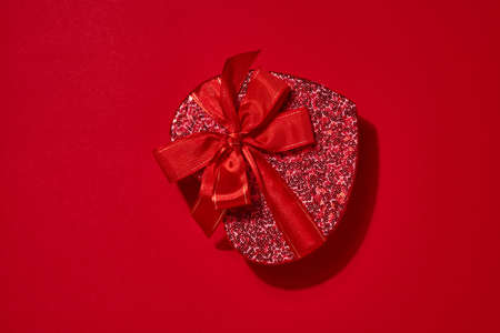 Open red heart box, ribbon and scattered hearts nearbyon scarlet background. Valentines day postcard...