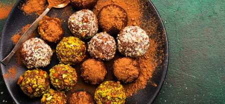 Variety of homemade dark chocolate truffles with cocoa powder, pistachios, almonds in dark brown...