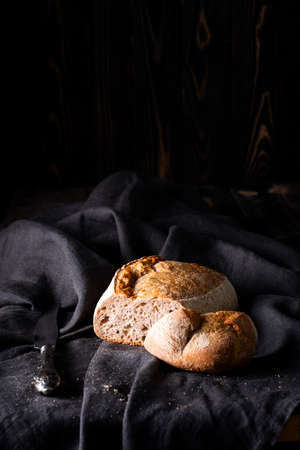 Freshly baked homemade sour dough bread on dark linen napkin, wooden background.