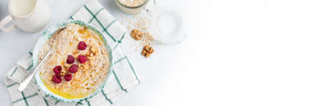 Oatmeal porridge with fresh raspberries, walnuts and butter in a ceramic plate on a light stone or concrete background. Selective focus.の写真素材