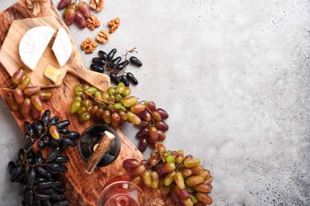 Two Wine bottles with grapes, slice cheese camembert, nut and wineglasses on old gray concrete table background with copy space. Red wine with vine branch. Wine composition on rustic style. Mock up.の写真素材