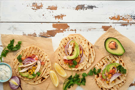 Mexican tacos with grilled chicken, avocado, corn kernels, tomato, onion, cilantro and salsa old white wooden table. Traditional Mexican and Latin american street food. Top view.の写真素材