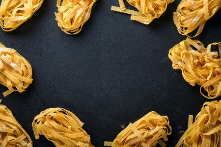 Tagliatelle. Homemade pasta, basil leaves, flour, pepper, olive oil and cherry tomato on dark black background. Food concept. Mock up. Horizontal with copy space.の写真素材
