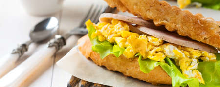 Sandwich stuffed with scrambled eggs, ham and lettuce leaves on a light wooden background. Selective focus.の写真素材