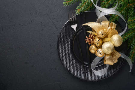 Served christmas table setting empty black ceramic plate on dark background Christmas Decoration. Holiday Decorations with gold baubles and fir branches on dark black background Border design Top viewの写真素材