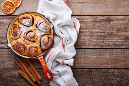 Cinnabon cinnamon rolls buns with pumpkin, nut, caramel and sugar cream iced on rustic wooden background table. Top view. Sweet Homemade Pastry christmas baking. Kanelbule - swedish dessert.の写真素材