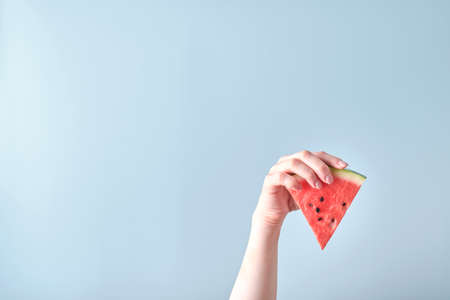 Female hand holds watermelon slice on blue background. Colorful hot summer holidays. Close up slices...