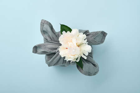 Spring eco-friendly gift wrapped in gray textile with one white peony flowers decor on blue....