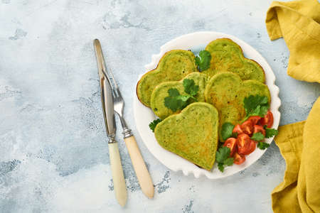 Spinach avocado pancakes in the shape of a heart with greek yogurt sauce and cherry tomatoes on white plate over light grey background. Breakfast food concept. Top view with copy space.の写真素材