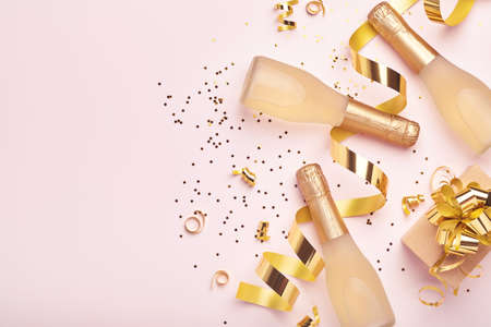 Champagne bottle, gift or present box and golden shiny sparkle star confetti on pink background. Christmas or New Year composition or card. Celebration flat lay. Party creative concept. Top view.の写真素材