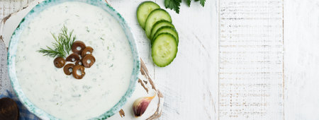 Traditional Greek sauce Tzatziki. Yogurt, cucumber, dill, garlic and salt oil in a ceramic bowl on a light wooden background. Rustic style. Selective focus. Top viewの写真素材
