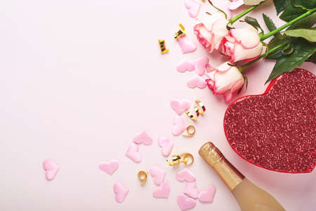 Pink roses flowers, champagne, gift, golden ribbons and confetti red hearts on pink background. Top view flat lay with space for your greetings. Valentines day background and greeting card.の写真素材