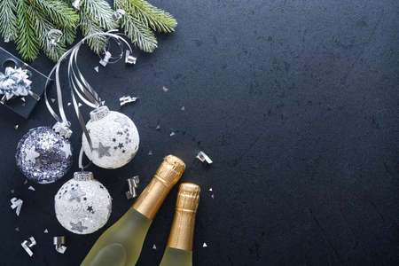 Christmas or New Year concept with black and silver baubles ball, gift box and champagne with decorated silver metallic ribbon on black background. Happy New Year 2022. Mock up.の写真素材